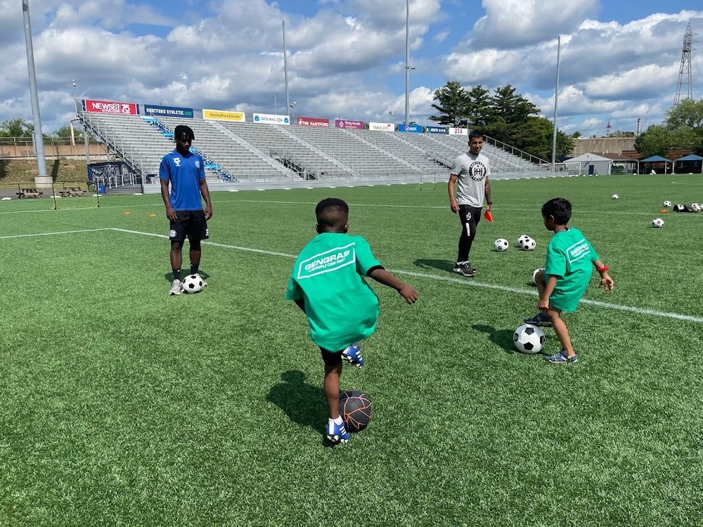 Students playing soccer on field with Hartford Athletic players